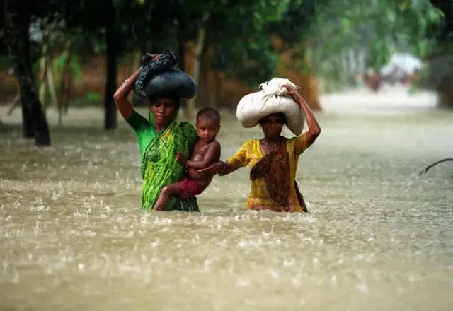 Two women carrying bundles through flood water
